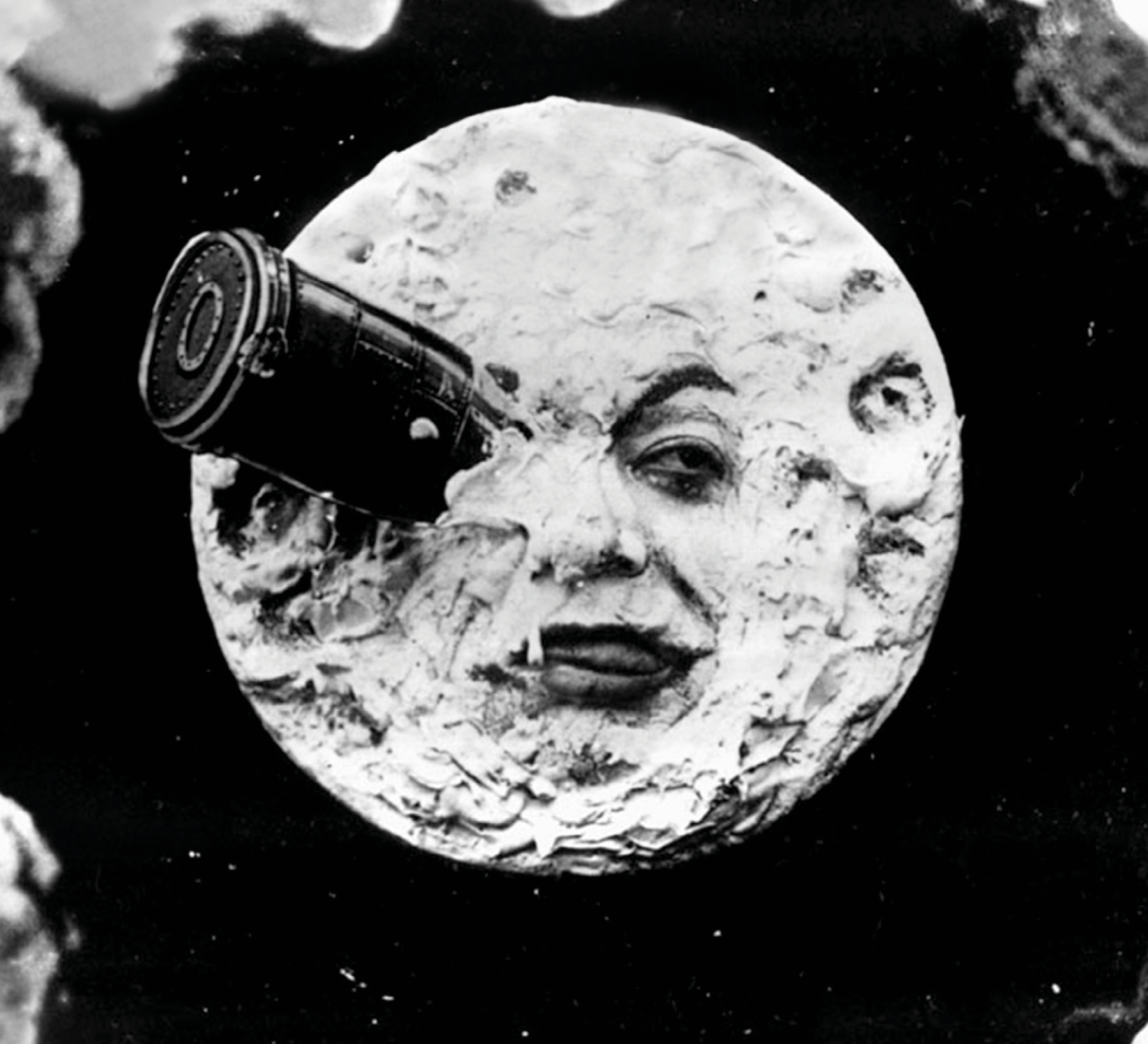 Fotograma. Imagem em preto e branco de filme cinematográfico antigo em que a Lua apresenta um rosto humano com expressão aborrecida porque está com uma cápsula espacial entalada dentro de um dos olhos.