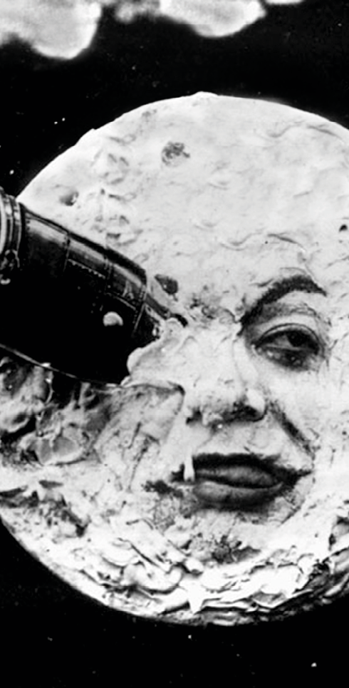 Fotograma. Imagem em preto e branco de filme cinematográfico antigo em que a Lua apresenta um rosto humano com expressão aborrecida porque está com uma cápsula espacial entalada dentro de um dos olhos.