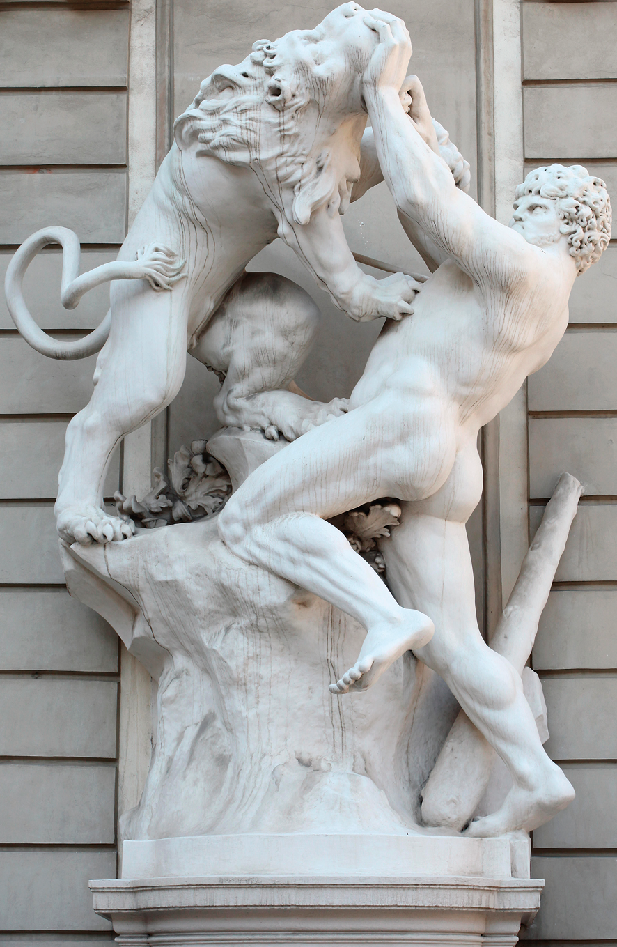 Fotografia.  Escultura em mármore. À esquerda, um leão com uma das patas sobre o peito de Hércules, um homem nu com cabelos cacheados e músculos destacados. Ele está inclinado para trás, lutando contra o leão e segurando a boca dele  dele com as mãos.  Ao lado de Hércules um bastão.