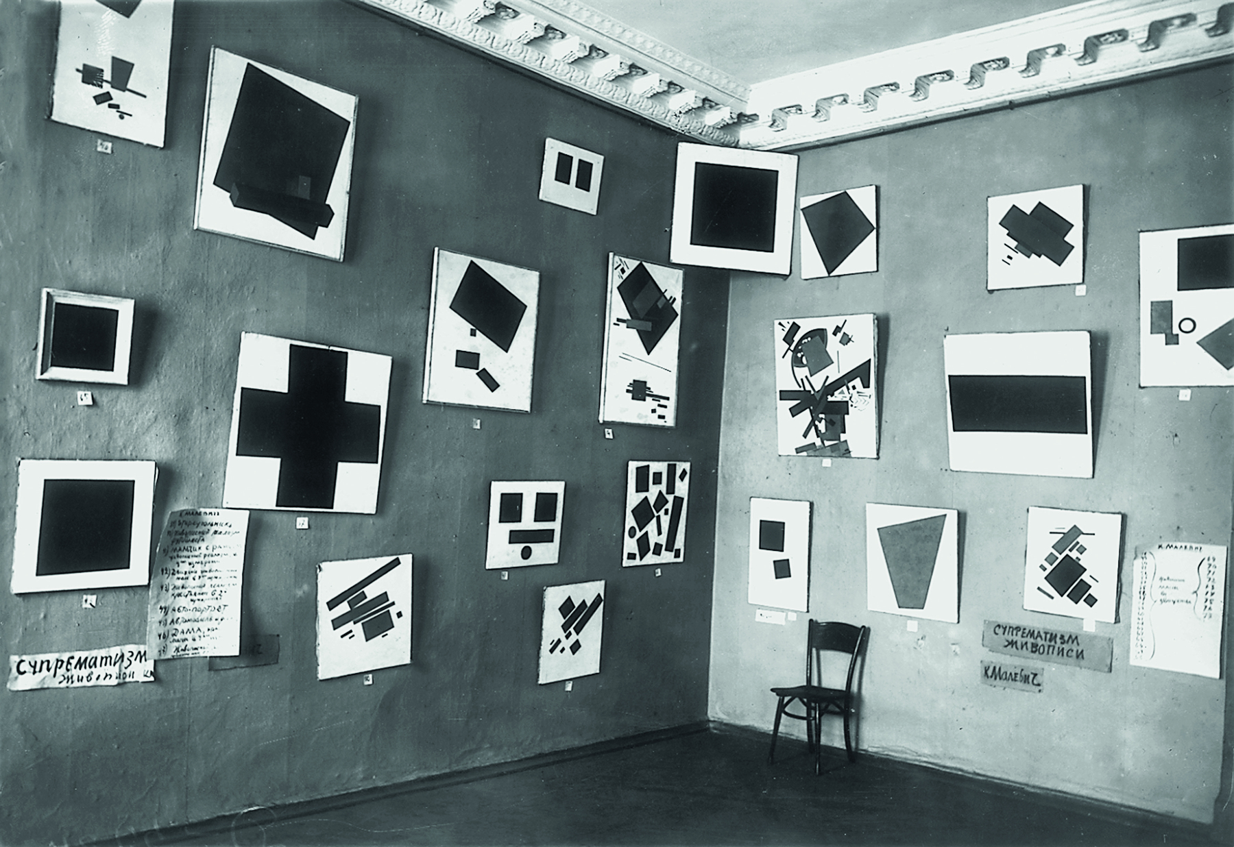 Fotografia em preto e branco. Parede onde estão expostos quadros com formas geométricas diversas.