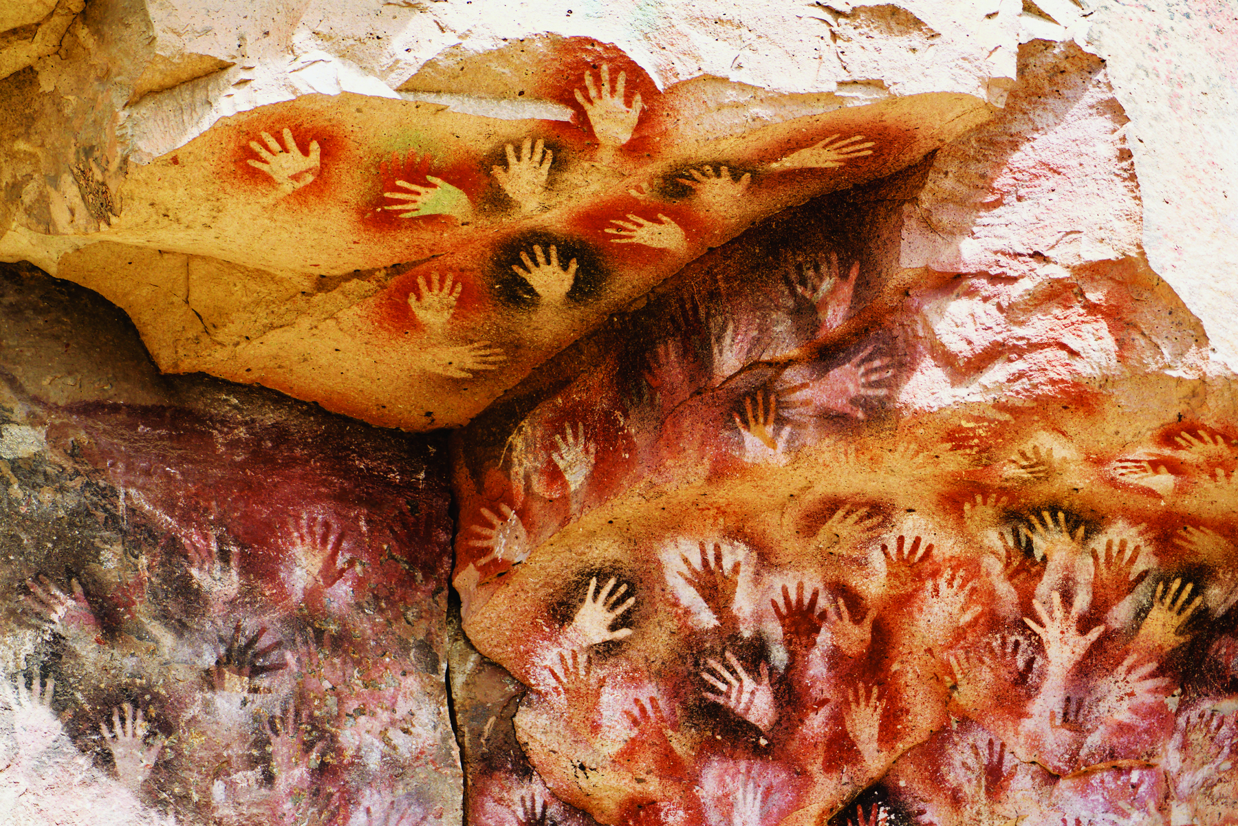Fotografia. Pinturas rupestres feitas com marcas de mãos na rocha.