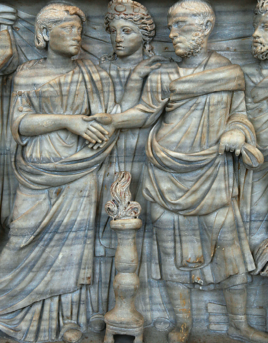 Escultura. Imagem em alto relevo feito em pedra. Representa duas pessoas apertando as mãos. Atrás delas, outra pessoa observa.