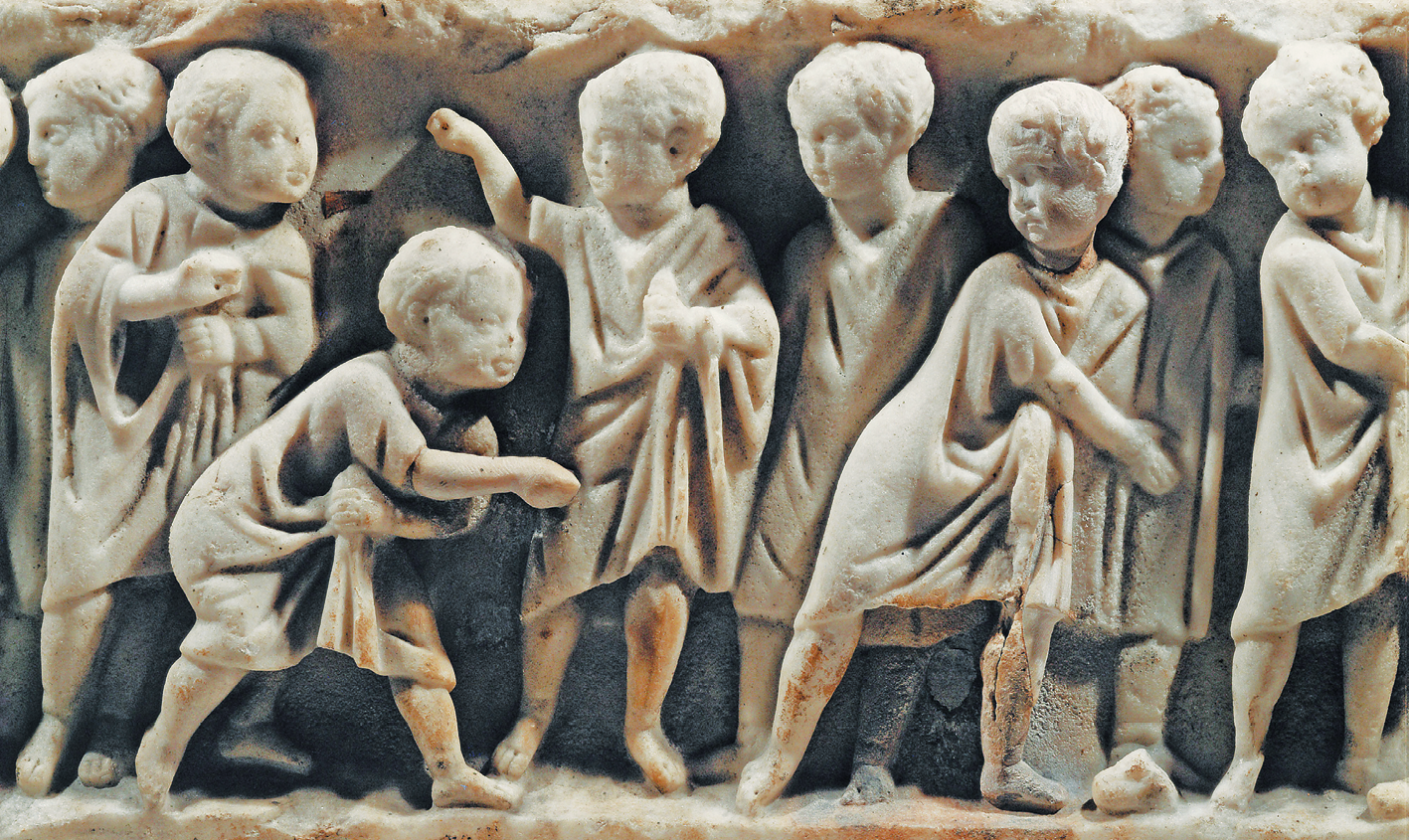Escultura. Imagem de crianças esculpida em alto relevo, em mármore. Elas usam túnicas. Algumas estão olhando para o lado. Outras estão inclinadas, com a mão à frente do corpo, como se arremessassem algum objeto.