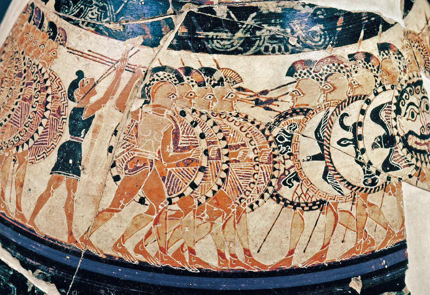 Fotografia. Parte externa de um vaso com pintura representando soldados com escudos e flechas se enfrentando. A superfície tem algumas rachaduras.