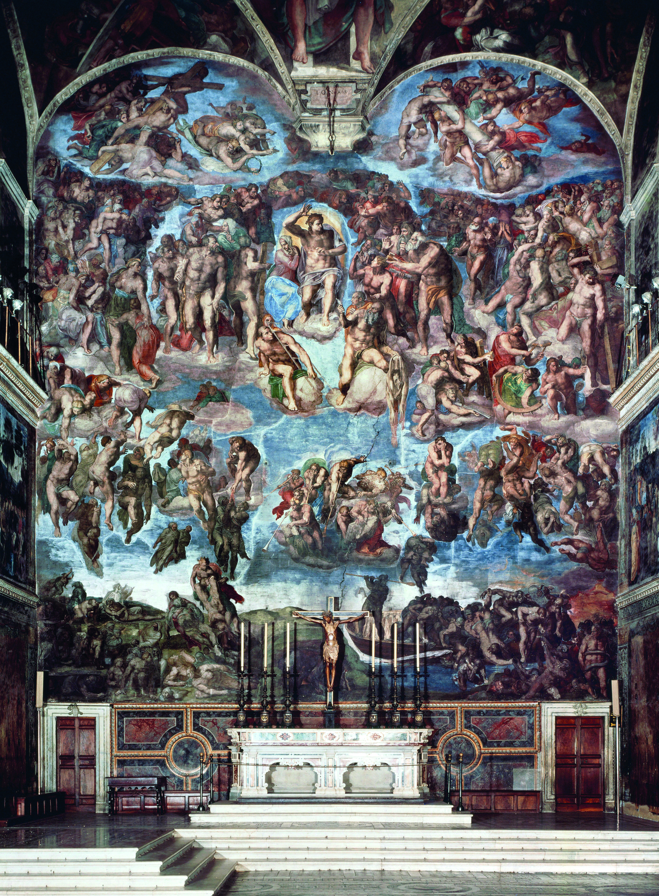 Fotografia. No centro, um altar de pedra clara com degraus à frente. Atrás e no teto uma grande pintura, com fundo azul e nuvens, de grupo de pessoas em situações diversas, representando cenas do Antigo Testamento.