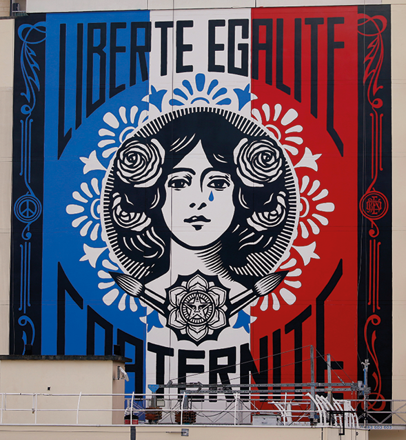 Fotografia. Mural pintado nas cores da bandeira da França: azul, branco e vermelho. No centro, a imagem do rosto de uma mulher com o cabelo enfeitado com rosas. Ao redor dela as palavras, LIBERTÉ, EGALITÉ, FRATERNITÉ. Nas bordas do mural ornamentos desenhados.