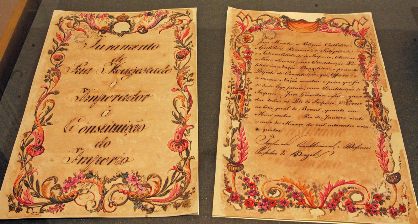 Fotografia. Duas páginas de um manuscrito. São amareladas e enfeitadas nas bordas por desenhos florais. No centro, texto escrito com letra de mão.