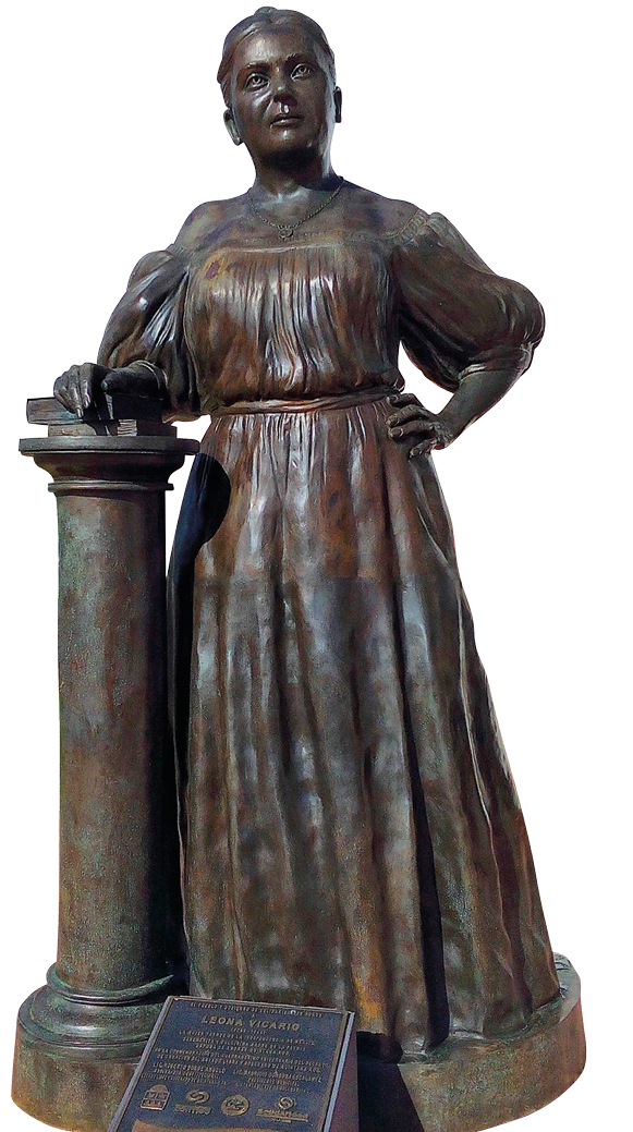 Escultura. Estátua de metal de uma mulher de vestido longo. Tem olhos pequenos e cabelo arrumado para trás. Uma mão está apoiada na cintura a outra está apoiada sobre livros que estão em um pilar.