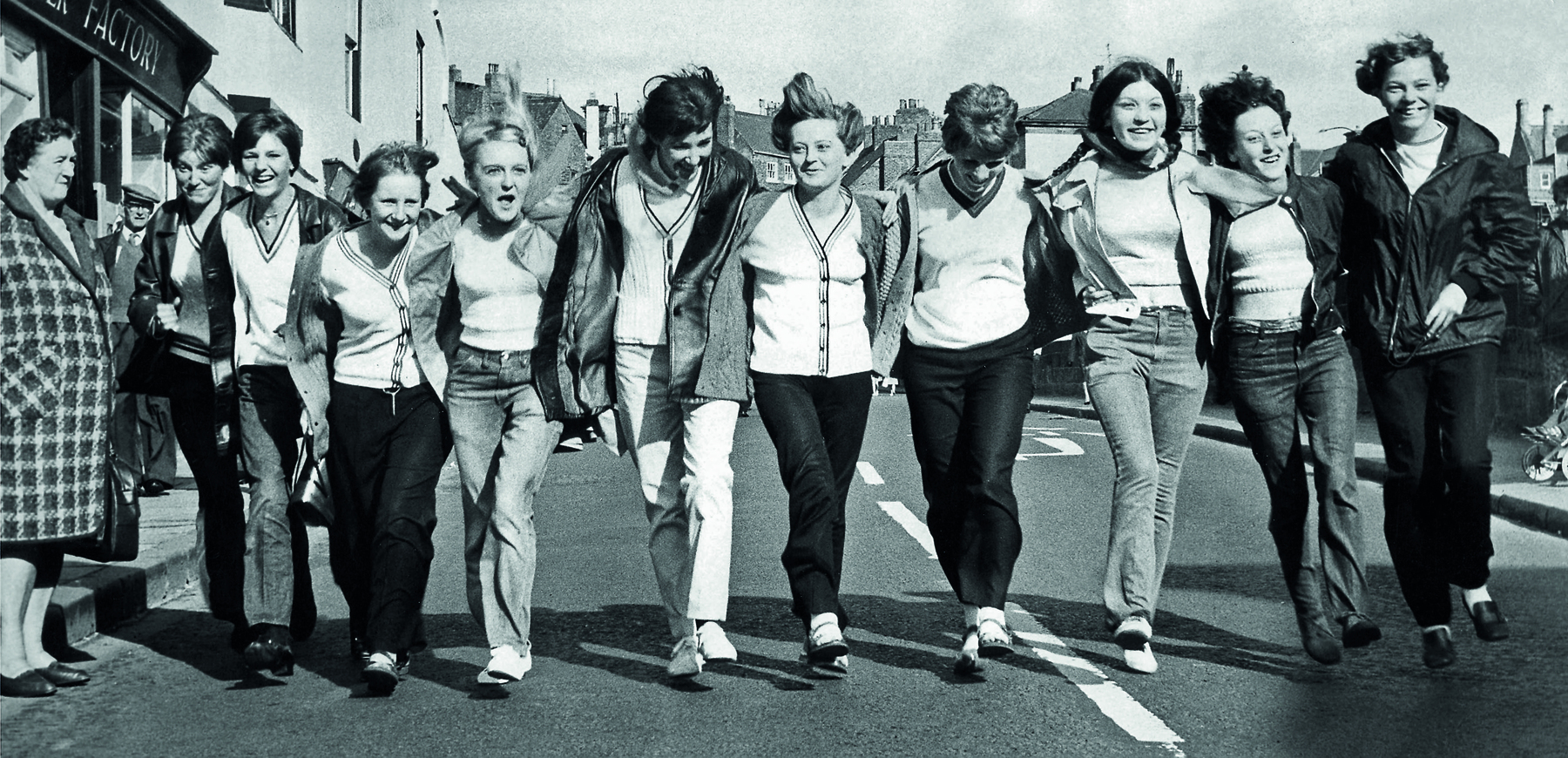 Fotografia em preto e branco. Grupo de jovens sorridentes andando abraçados, lado a lado.