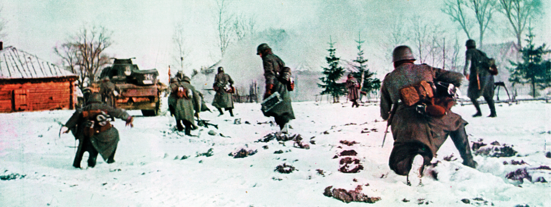 Fotografia colorizada. Soldados andando sobre uma camada densa de neve. Vestem sobretudo, capacete e carregam pequenas bolsas no cinto. Ao fundo, um tanque de guerra ao lado de uma casa.