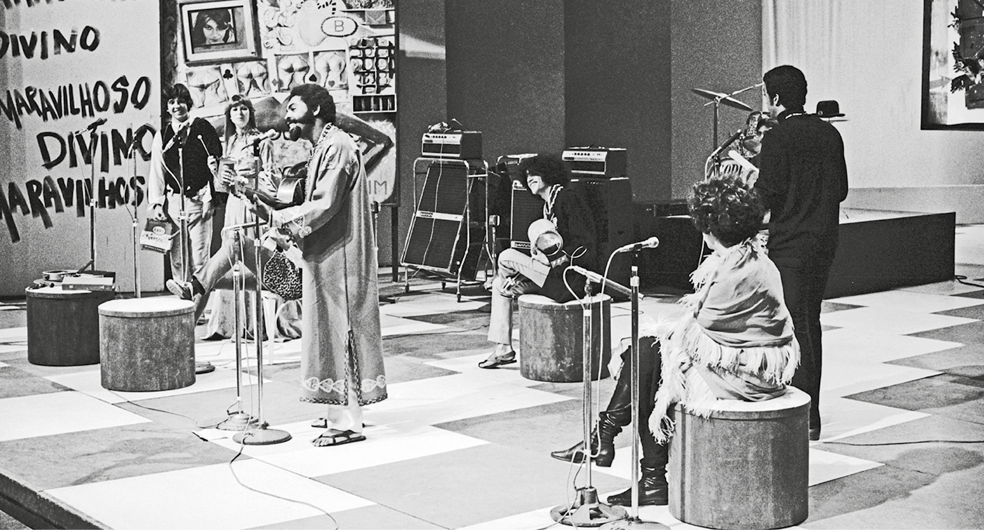 Fotografia em preto e branco. Grupo de pessoas em uma apresentação musical em um auditório de programa de televisão.