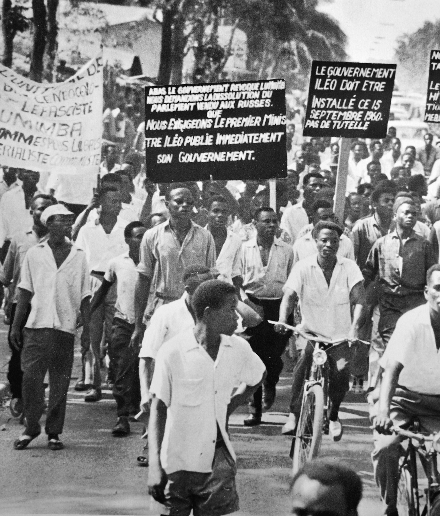 Fotografia em preto e branco. Grupo de pessoas reunidas em uma manifestação. Carregam cartazes com escritos em francês.