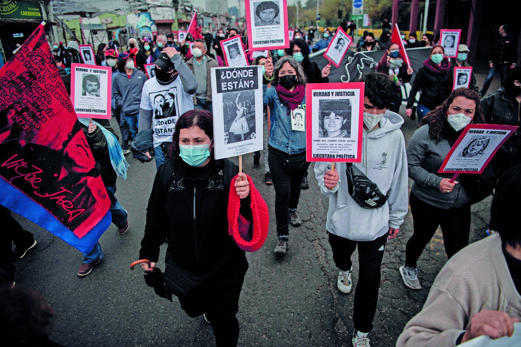 Fotografia. Manifestantes usando máscaras de proteção facial carregam cartazes com fotos de pessoas diferentes. Muitos dos cartazes apresentam uma frase cuja tradução é Onde estão?