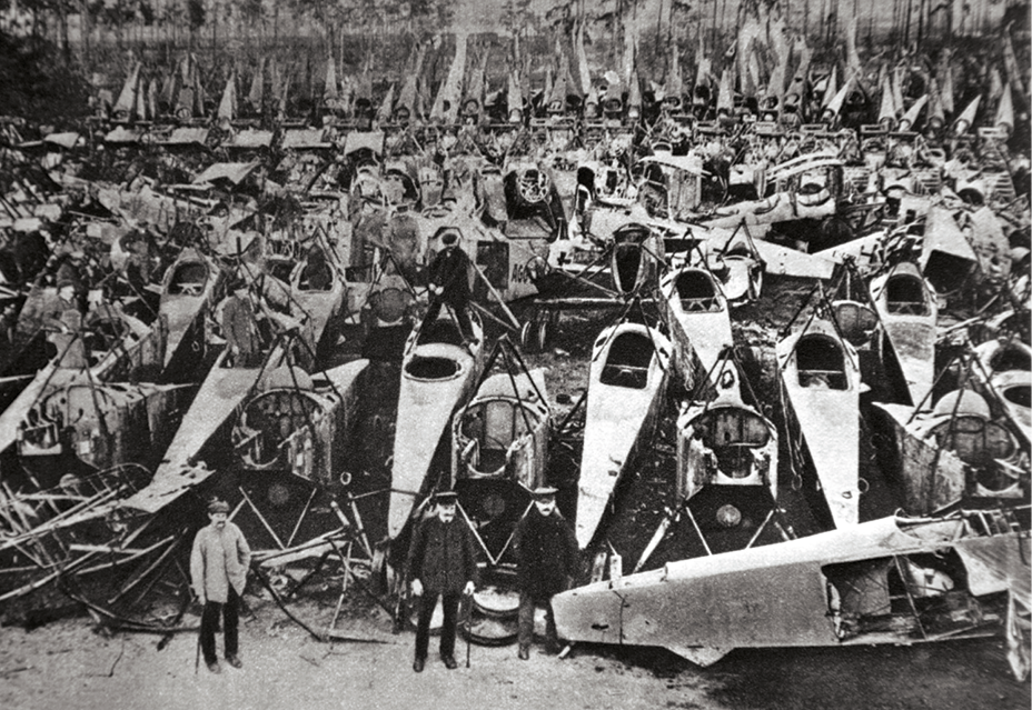 Fotografia em preto e branco. Homens em meio a carcaças de veículos e equipamentos abandonados.