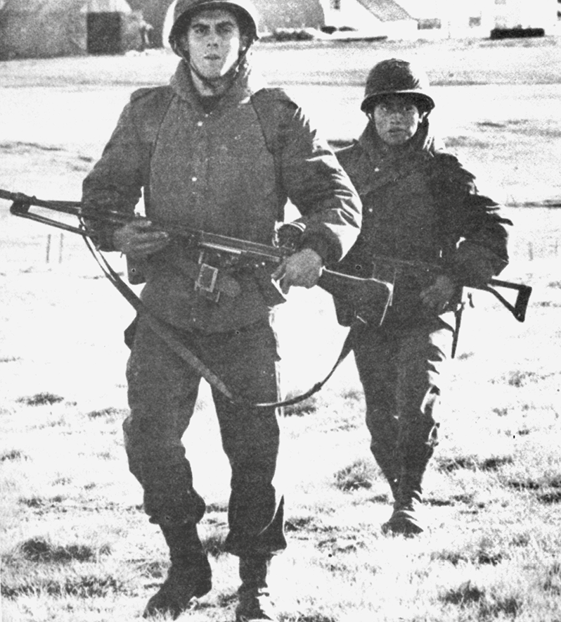 Fotografia em preto e branco. Dois soldados agasalhados caminham com a arma em mãos.