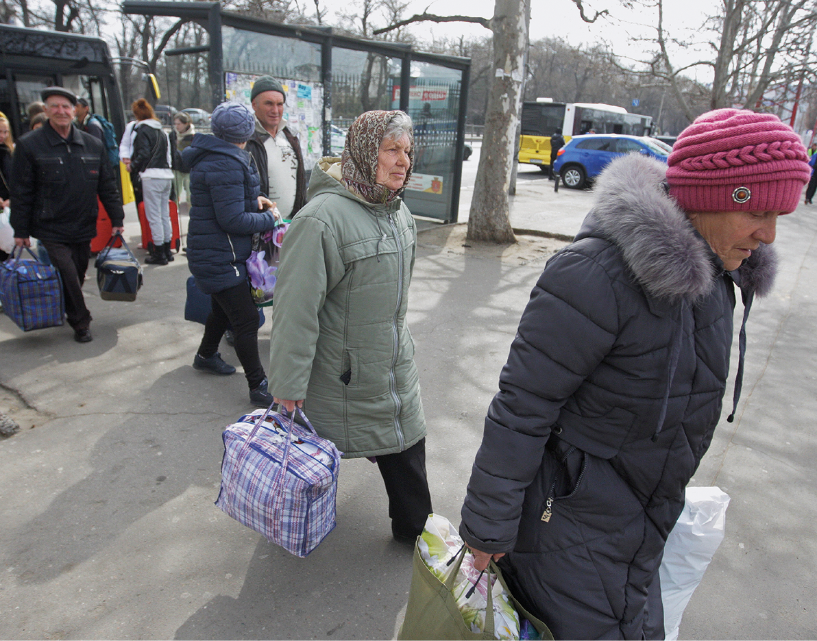 Fotografia. Algumas pessoas agasalhadas com casacos em gorros descem de um ônibus carregando algumas malas e sacolas.