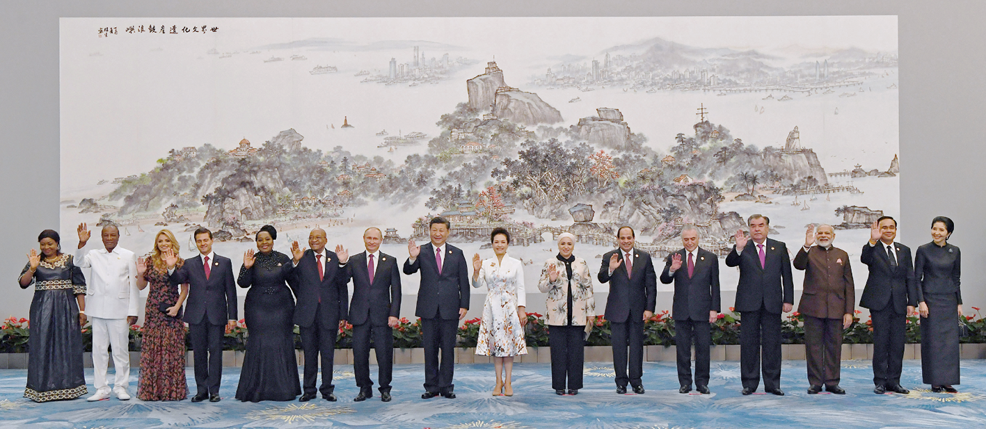 Fotografia. Chefes de Estado posando para foto, alinhados lado a lado. Homens e mulheres acenando com uma das mãos.