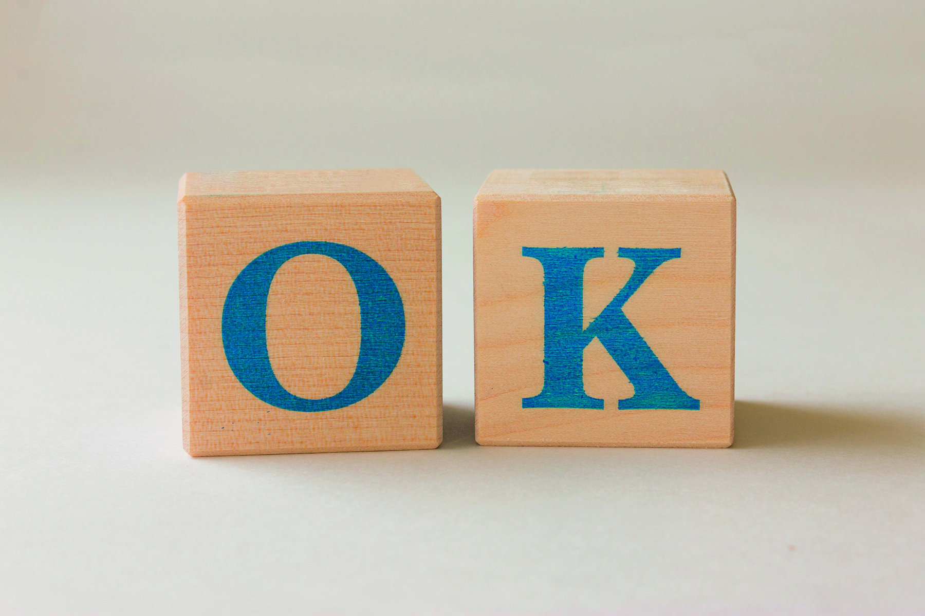 Fotografia. Dois cubos de madeira em bege, cada um com uma letra em azul, formando a palavra: OK.