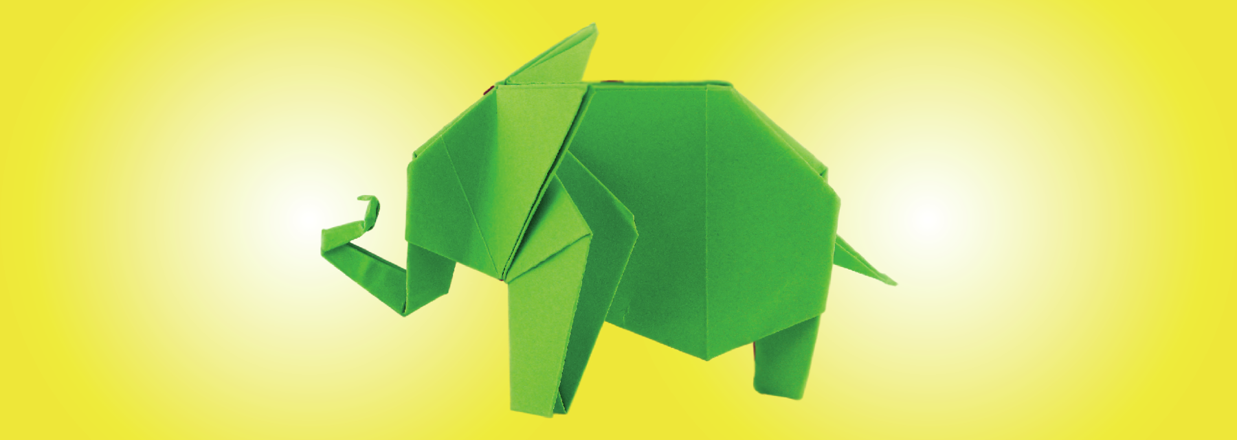 Fotografia. Dobradura de um elefante de cor verde, com o corpo para a esquerda, com a tromba para cima, com uma ponta e rabo na outra ponta, pequeno.
