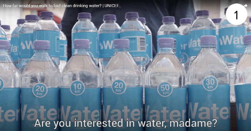 Captura de tela. Dezenas de garrafas plásticas transparentes com água, tampa e embalagem azul claro. Na parte inferior, legenda do vídeo que diz: Are you interested in water, madame?