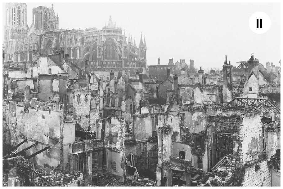 Fotografia dois. Em preto e branco. Vista geral da mesma cidade francesa, desta vez em meados de 1945. Alguns prédios estão danificados ou em ruínas.