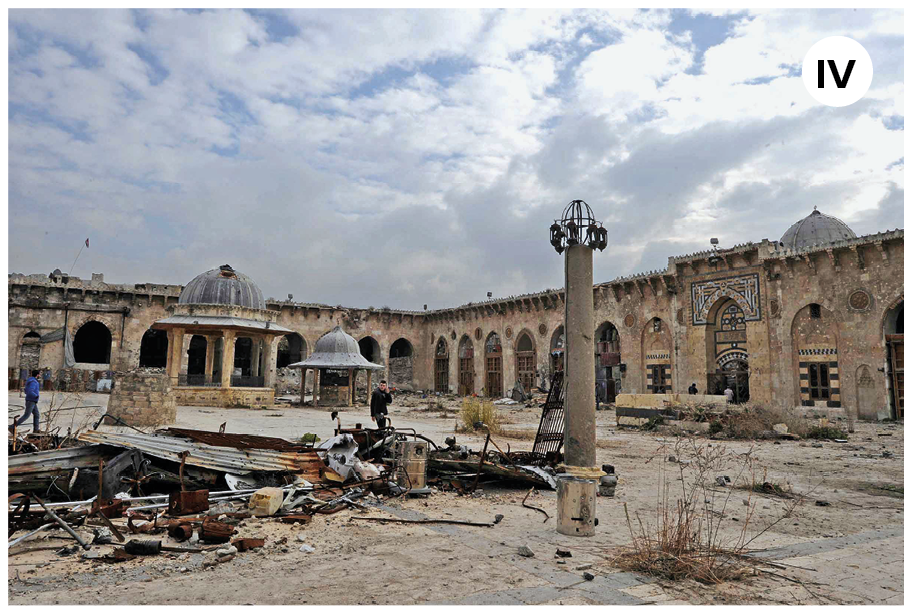 Fotografia quatro. Vista geral da mesma mesquita em ruinas sobre o chão e ao fundo, uma torre na vertical em bege e parede com paredes e os dois coretos de teto cinza. Na parte superior, céu azul-claro e nuvens brancas.