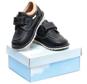 Fotografia. Par de sapatos infantis pretos novos com velcro e sola cinza-claro sobre caixa de papel azul. O calçado direito está apoiado no esquerdo.