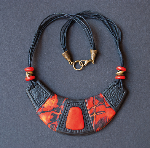 Fotografia. Um colar preto com a parte inferior com ornamento em formato de letra U em preto e laranja.