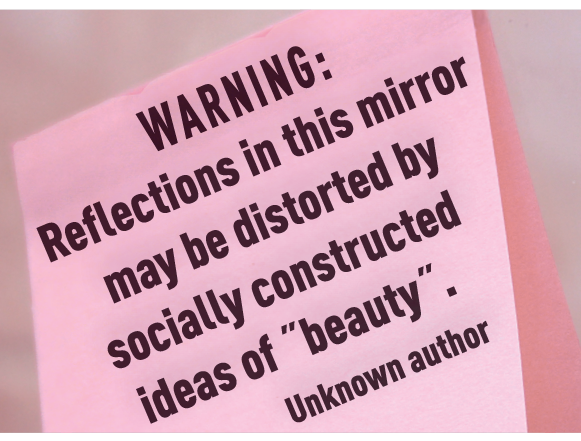 Fotografia. Nota em papel rosa com texto:  WARNING: Reflections in this mirror may be distorted by socially constructed ideas of beauty. Unknown author."