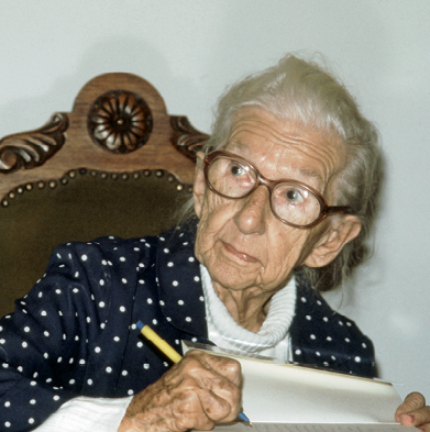 Fotografia. Cora Coralina, senhora de pele clara, cabelo branco e queixo oval. Usa óculos de armação grande.