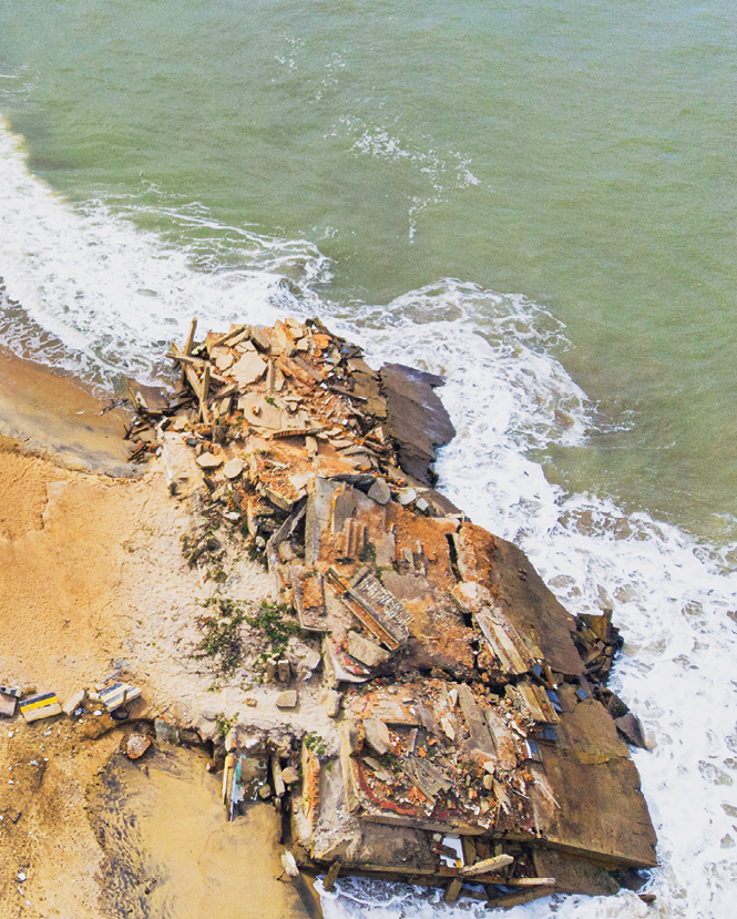 Fotografia. Vista aérea dos destroços de uma casa a beira mar.