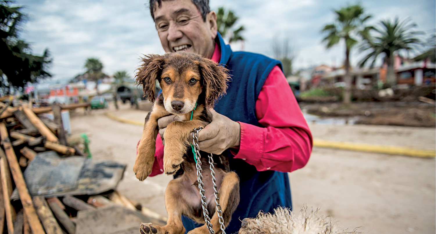 Fotografia. Jorge Castro, homem de aproximadamente 50 anos. Tem cabelo curto, pele clara. Nariz grande e olhos pequenos. Segura um cachorrinho de pelo marrom nas mãos.