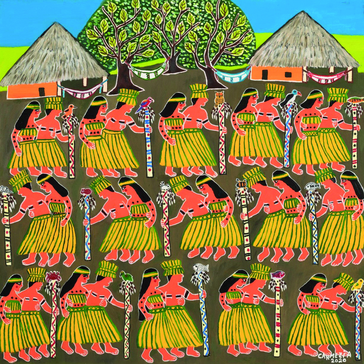Obra de arte. Casais indígenas em um ritual, alinhados em três filas. Os homens vestem um longo saiote e seguram um cajado com uma ave na ponta. As mulheres usam longo saiote e cobertura no busto. Eles têm pinturas pelo corpo. Ao fundo, redes de descanso penduradas entre as árvores e ocas.