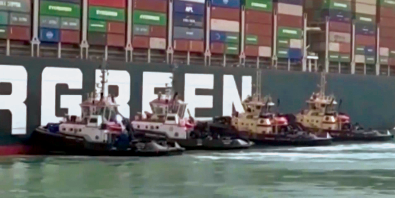 Fotografia. Destaque para pequenos barcos na lateral de um navio cargueiro.