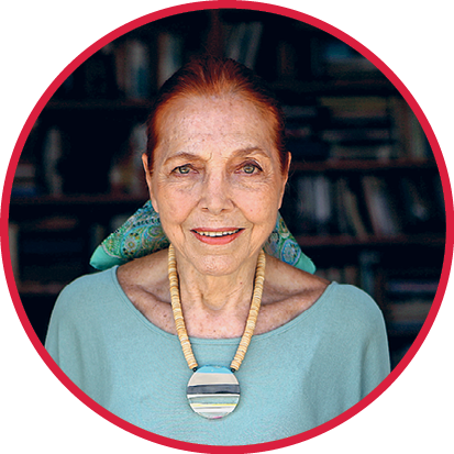 Fotografia. Marina Colasanti, senhora de cerca de 80 anos, branca de cabelos ruivos. Tem olhos pequenos e lábios rosados. Usa um grande colar com um pingente circular.