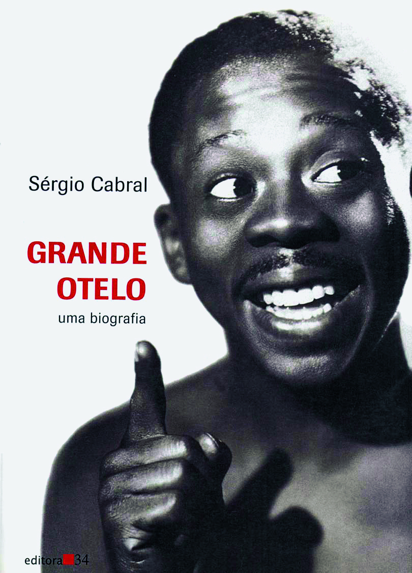 Capa de livro. Ocupando toda a capa fotografia de um rapaz negro, de cabelo curto, sorridente. Usa bigode fino. Está apontando para cima, na direção do título: GRANDE OTELO uma biografia.