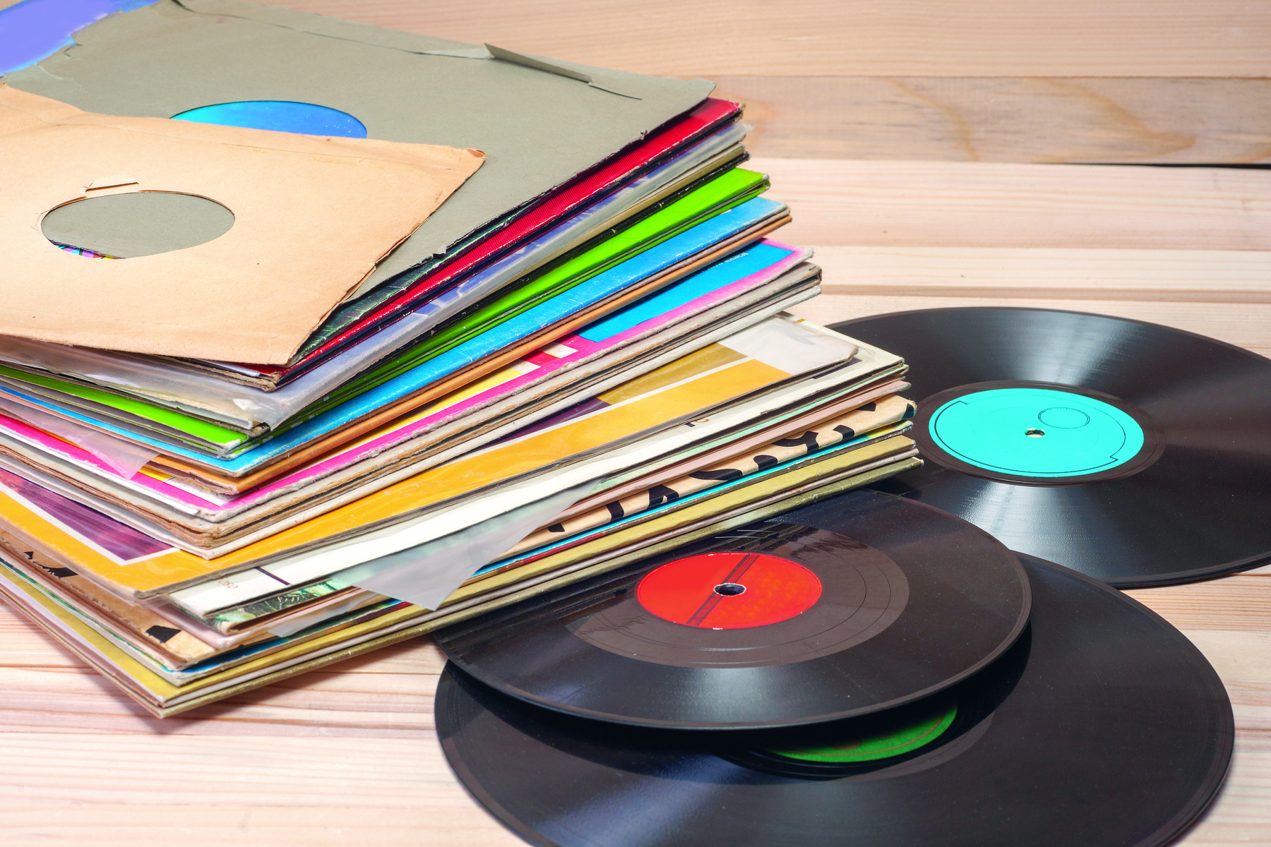 Fotografia. Capas de discos empilhadas uma sobre a outra e sobrepostas a três  discos pretos, com a parte central nas cores azul, vermelho e verde.