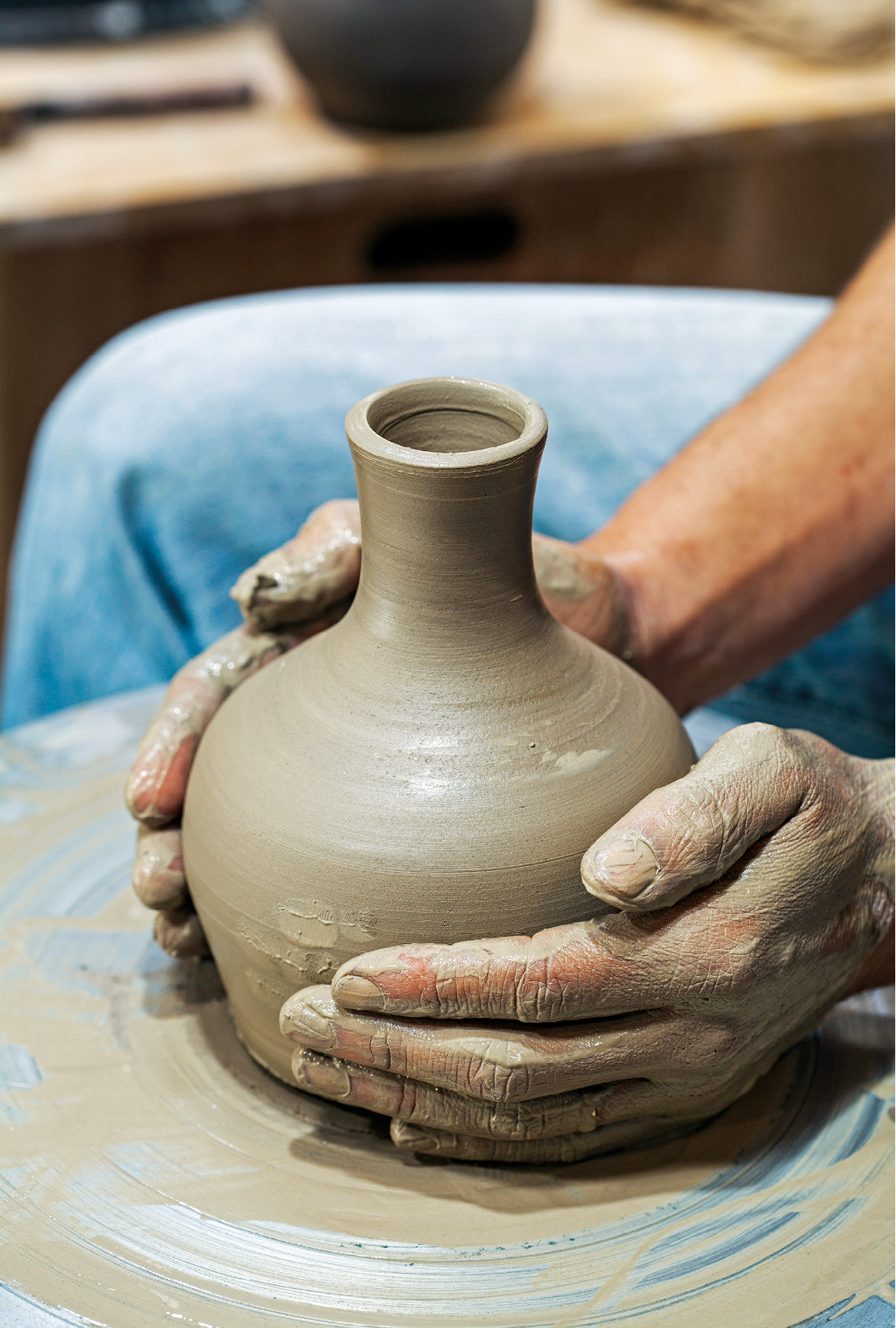 Fotografia. Destaque para duas mãos manipulando um vaso de cerâmica em produção.