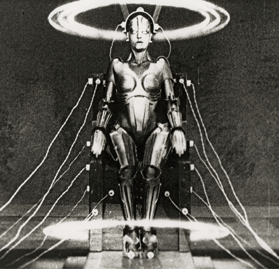 Fotografia em preto e branco de cena de filme. Um robô cinza com forma humana está sentado em uma poltrona; ao lado da poltrona há linhas claras com pontos de choque na cadeira e na cabeça do robô. Acima dele, há um círculo branco.