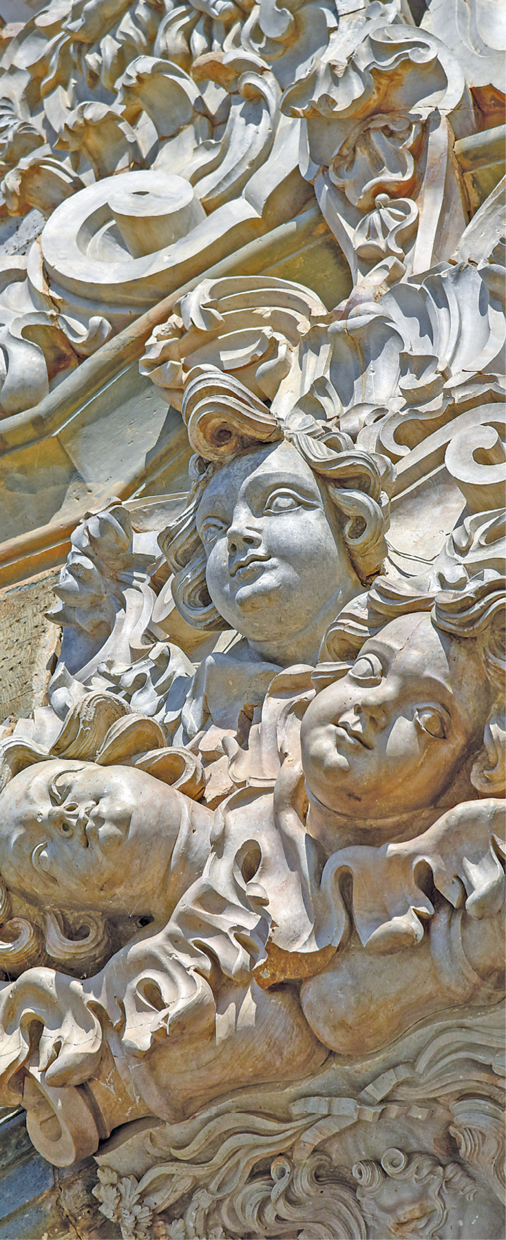 Fotografia. Destaque para esculturas em relevo, feitas com pedra-sabão. Diversos rostos humanos com cabelos ondulados estão esculpidos nela.