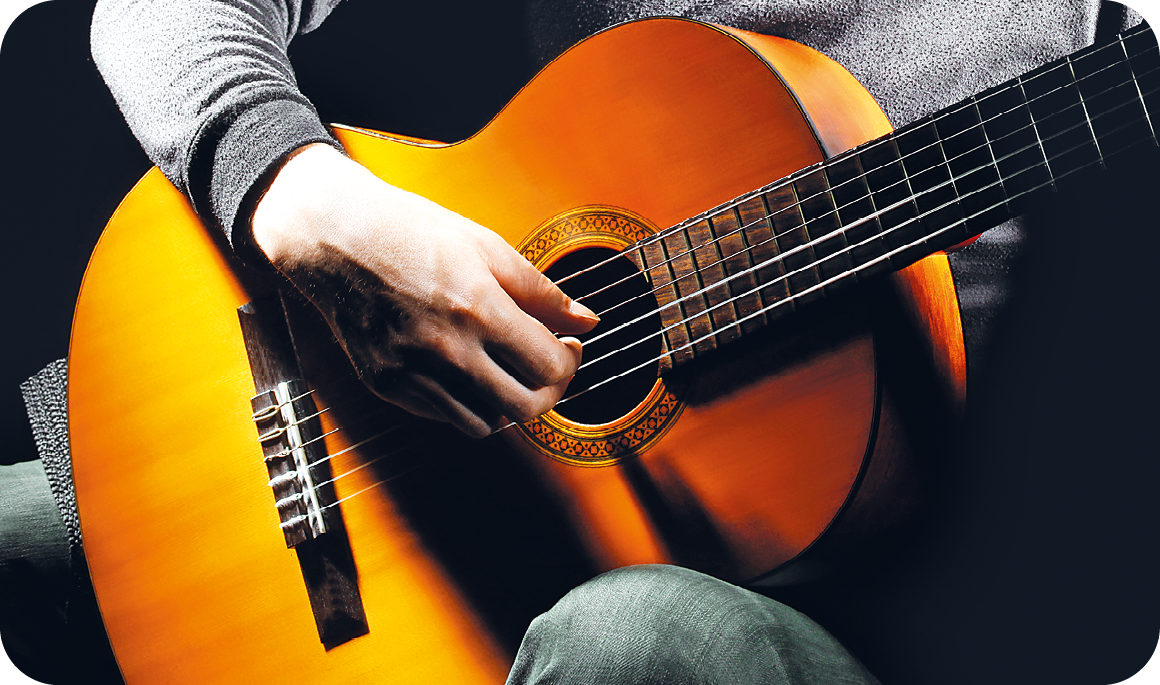 Fotografia. Destaque das mãos de uma pessoa que toca um violão de madeira.