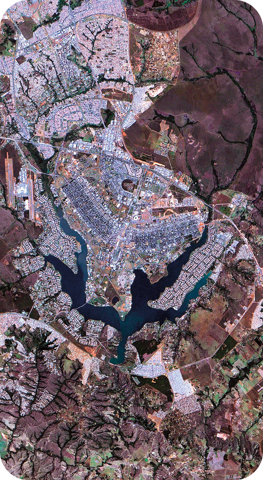 Fotografia. Vista aérea de uma cidade cercada por vegetação e porções de água.