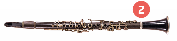 Fotografia número 2. Instrumento de sopro cilíndrico com poucas chaves ao longo do corpo e um tubo grosso em uma da extremidades.
