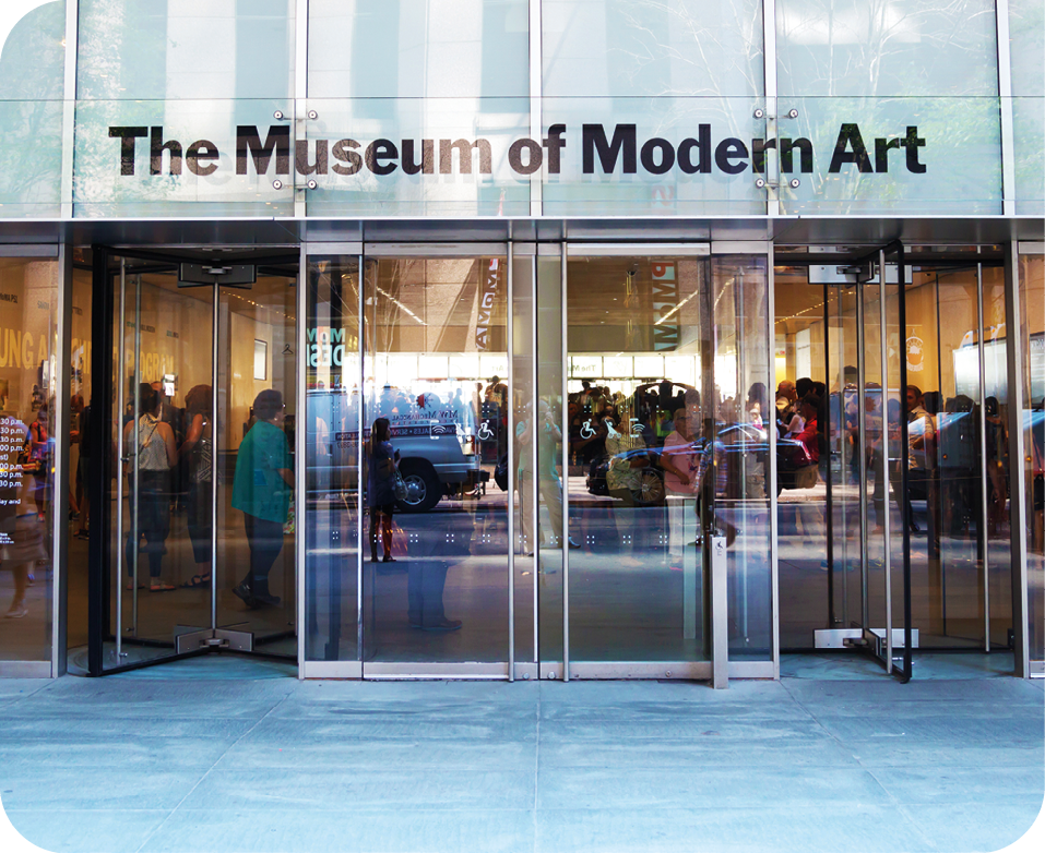 Fotografia. Destaque para as portas  envidraçadas de um prédio que apresenta a inscrição 'THE MUSEUM OF MODERN ART'. Por trás da porta, algumas pessoas em pé.