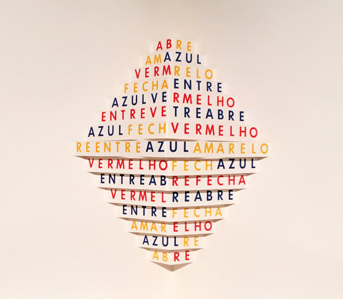 Poema concreto. Com letras nas cores azul, vermelho e amarelo, há uma composição que forma um losango a partir da junção de pequenas frases em cada linha: ABRE; AMAZUL; VERMRELO; FECHA ENTRE; AZUL VERMELHO; ENTREVE TREABRE; AZUL FECHVERMELHO; REENTRE AZUL AMARELO; VERMELHO FECH AZUL; ENTREABRE FECHA; VERMEL REABRE; ENTRE FECHA; AMARELHO AZULRE; ABRE.