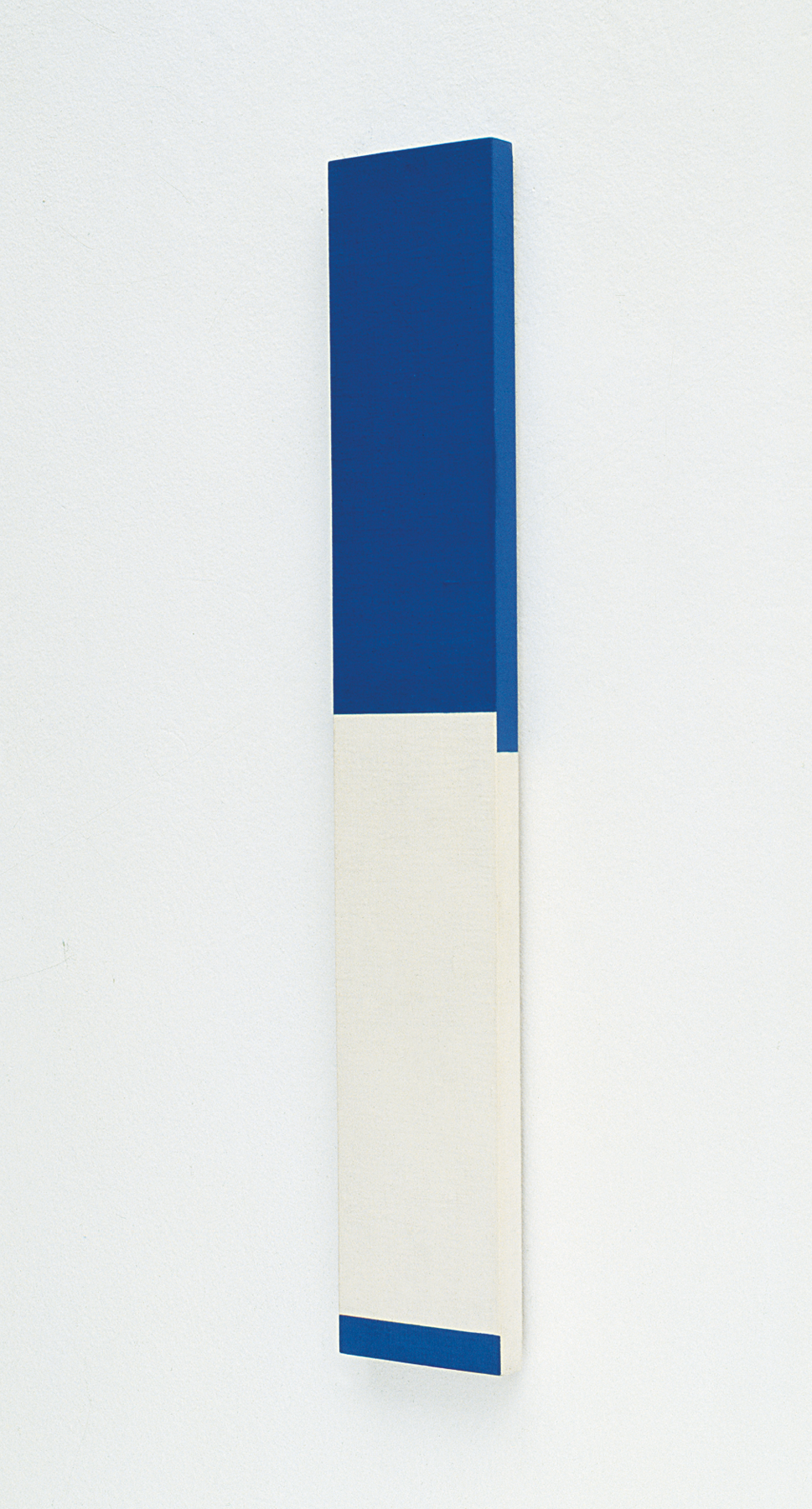 Pintura. Uma barra retangular verticalizada com a parte superior pintada de azul e a parte inferior pintada de branco com uma pequena barra horizontal em cor azul na extremidade inferior.
