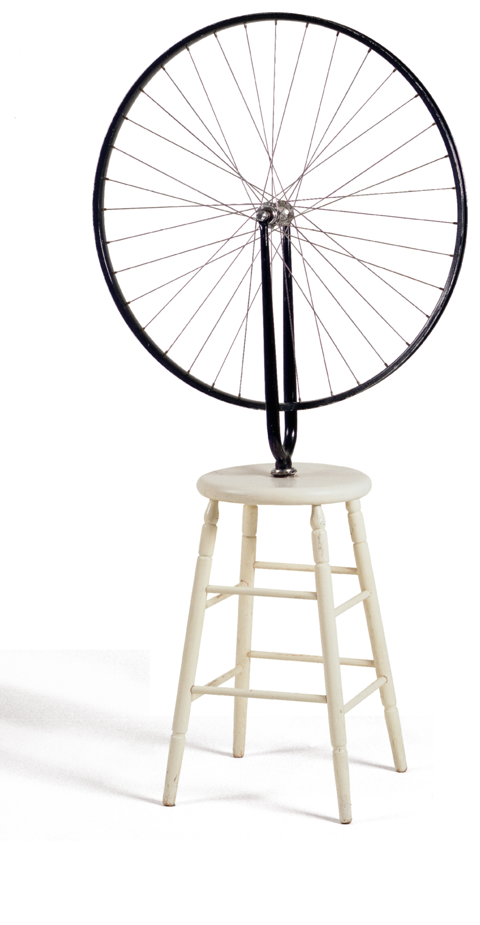 Escultura. Sobre uma banqueta branca, há uma roda de bicicleta preta apoiada num suporte sobre o assento.