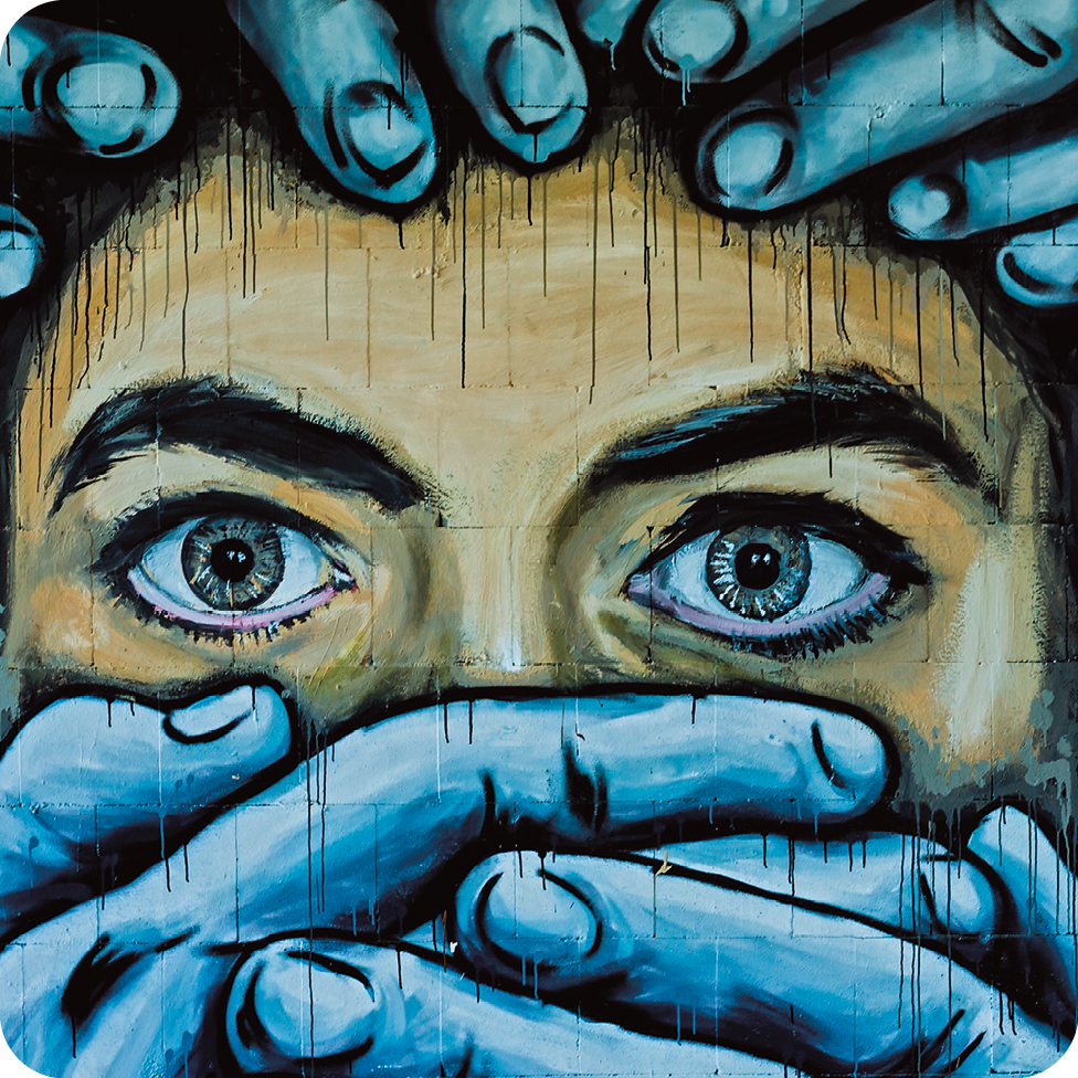 Fotografia. Destaque de grafite que apresenta muitos dedos em tons de azul ao redor da cabeça de uma pessoa e cobrindo sua boca. Estão visíveis apenas a testa e os olhos claros. Nas partes laterais esquerda e direita, há uma mão com os dedos fechados e vista parcialmente.