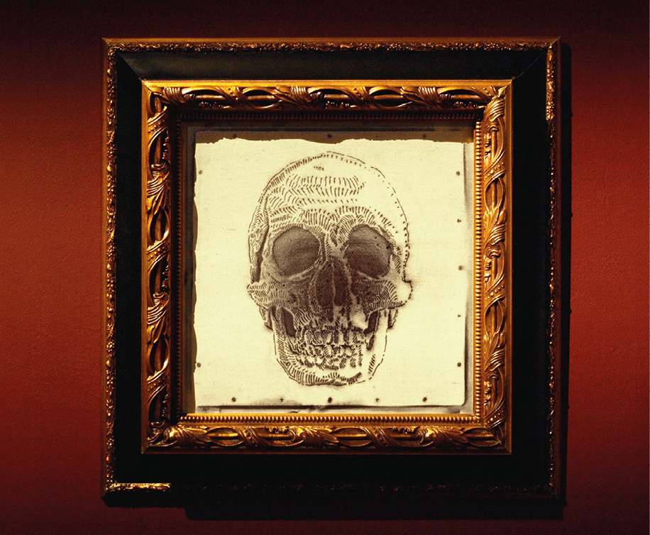 Fotografia. Pintura emoldurada em dourado e preto que apresenta o esqueleto de um rosto humano com a parte central esfumaçada.