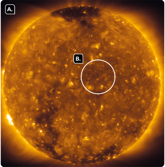 Fotografia.  Marcado pela letra A, o Sol, grande esfera, amarelada com manchas mais escuras, com contorno amarelo brilhante. E marcado pela B há um destaque de um círculo ao centro do Sol.